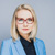 Professional portrait of a blonde woman wearing glasses and a blue blazer, looking at the camera.